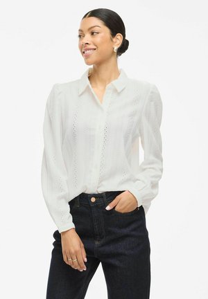 Witte blouse met knopen, gemaakt van textuurstof, met verticale uitsnijdpatronen, pofmouwen en een klassieke kraag. Gepaard met donkere jeans.