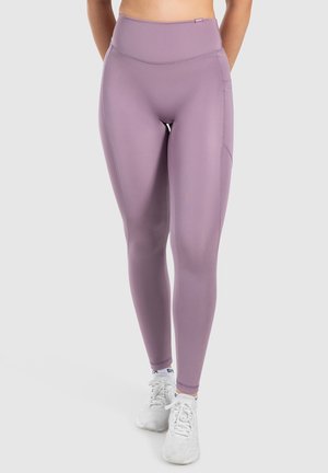 Fioletowe legginsy z wysokim stanem z elastycznego materiału, charakteryzujące się gładką teksturą i detalami szwów. Noszone z białymi butami sportowymi.