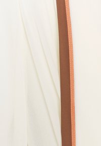 Ljus krämfärgad tyg med en mjuk textur, med en brun vertikal panel accentuerad av en tunn orange kant för kontrast.