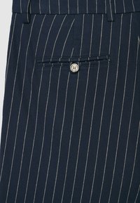 Pantaloni blu navy a righe sottili, con una tasca posteriore con bottone, realizzati in un tessuto strutturato con righe bianche a contrasto.