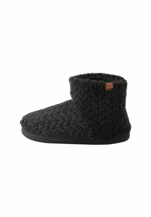 Schwarze gestrickte Knöchelboot-Slipper mit einem strukturierten Muster, weichem Material und einem braunen Lederakzentetikett an der Seite. Gummisohle.