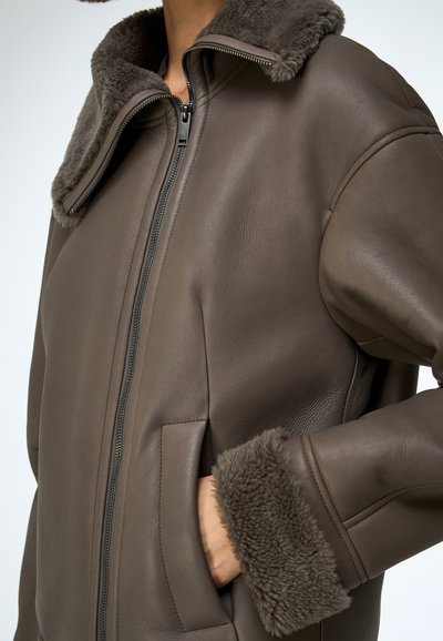 Hnedá kožená bunda s mäkkým kožušinovým golierom a manžetami, so zipsovým zapínaním a bočnými vreckami. Hladká textúra, elegantný strih.