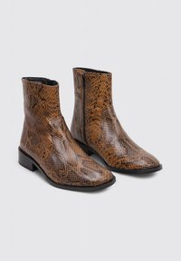 Bottines à imprimé serpent marron avec une finition lisse et brillante, des zips sur le côté et un petit talon block. Présente un design à bout pointu.