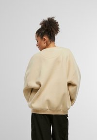 Felpa oversized beige con scollatura rotonda, spalle basse e polsini a coste. Tessuto morbido, abbinata a pantaloni cargo neri.
