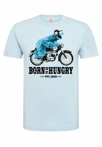 Hellblaues T-Shirt mit kurzen Ärmeln, das eine Grafik eines blauen, pelzigen Charakters auf einem Motorrad zeigt, mit dem Text "BORN TO BE HUNGRY" und "EST. 1966."