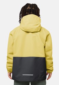 Veste imperméable avec une partie supérieure jaune et une partie inférieure noire, dotée de poignets élastiques et d'une capuche à cordon de serrage pour un ajustement personnalisable.