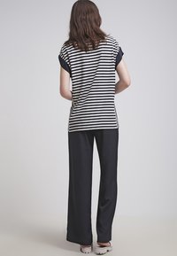 Woman standing facing away wearing a black and white striped short-sleeve top, black wide-leg pants, and white platform sandals.