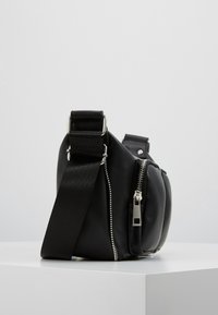 Borsa a tracolla nera con una texture liscia in pelle, dettagli con cerniera, tracolla regolabile e forma arrotondata. Dettagli in metallo tono argento.