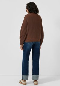 Brązowy sweter z prążkowanego dzianiny z wysokim kołnierzem, w zestawie z szerokimi dżinsami o szerokich nogawkach, wykończonymi podwiniętym dołem oraz beżowymi tenisówkami.