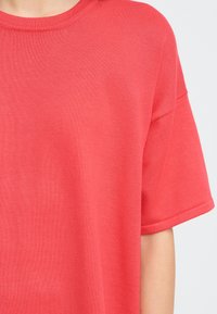 T-shirt corail à manches courtes en tissu doux. Doté d'un col rond et d'une coupe décontractée avec des détails côtelés au col et aux manches.