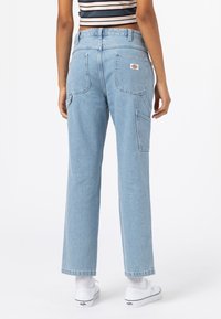 Světle modré džíny s uvolněným střihem, viditelnými zadními kapsami a logo na nášivce. Tkanina má mírnou strukturu a roztrhané lemy.