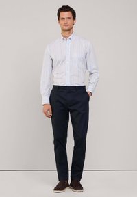 Gestreepte langearmige overhemd met knopen in lichte kleuren, gecombineerd met marineblauwe slim-fit broeken en Donkerbruine suède loafers.
