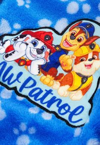 Blue fleece blanket featuring cartoon dogs from "Paw Patrol," with a large logo and playful expressions. Soft texture, polka dot background.