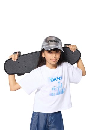 Kind met lang haar, een zilveren baseballpet en een witte cropped t-shirt. Houdt een zwarte skateboard met een textuurovervlak tegen haar schouder.