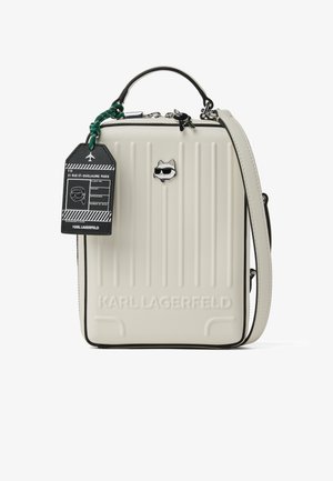 Κρεμ ορθογώνια τσάντα χειρός με κάθετες ραβδώσεις, επάνω λαβή, αποσπώμενο λουράκι, λογότυπο Karl Lagerfeld και μαύρη ταμπέλα αποσκευών με λευκό κείμενο.