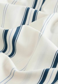 Bomullstyg med en vit bakgrund och blå och marinrandiga linjer, som visar en jämn textur och mjuka draperingsegenskaper.