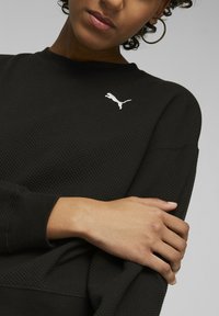 Czarny sweatshirt o fakturze waffle z okrągłym dekoltem i długimi rękawami. Z przodu znajduje się biały logo Puma na piersi. Miękka tkanina z luźnym krojem.
