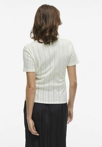 Korte mouwen crème top met verticale gestructureerde strepen en geometrische patronen, gecombineerd met zwarte broek. Glad materiaal.