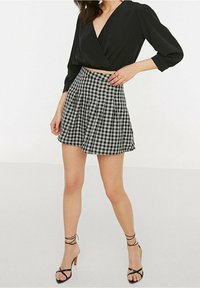 Blusa nera avvolgente con maniche a tre quarti abbinata a una gonna plissettata a quadretti bianchi e neri e sandali neri con cinturino.