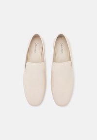 Bottines beiges en cuir lisse, dotées d'un bout arrondi et d'un design minimaliste, avec le logo Calvin Klein visible sur la semelle intérieure.