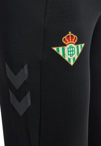 Pantalones deportivos negros hechos de un tejido elástico, con un logo de franjas verdes y blancas y una corona, y chevrons laterales en acabado mate.