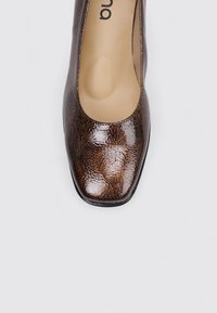 zapato de tacón cerrado marrón con un patrón, textura brillante, forma de punta cuadrada y plantilla beige. Presenta un diseño elegante y minimalista.