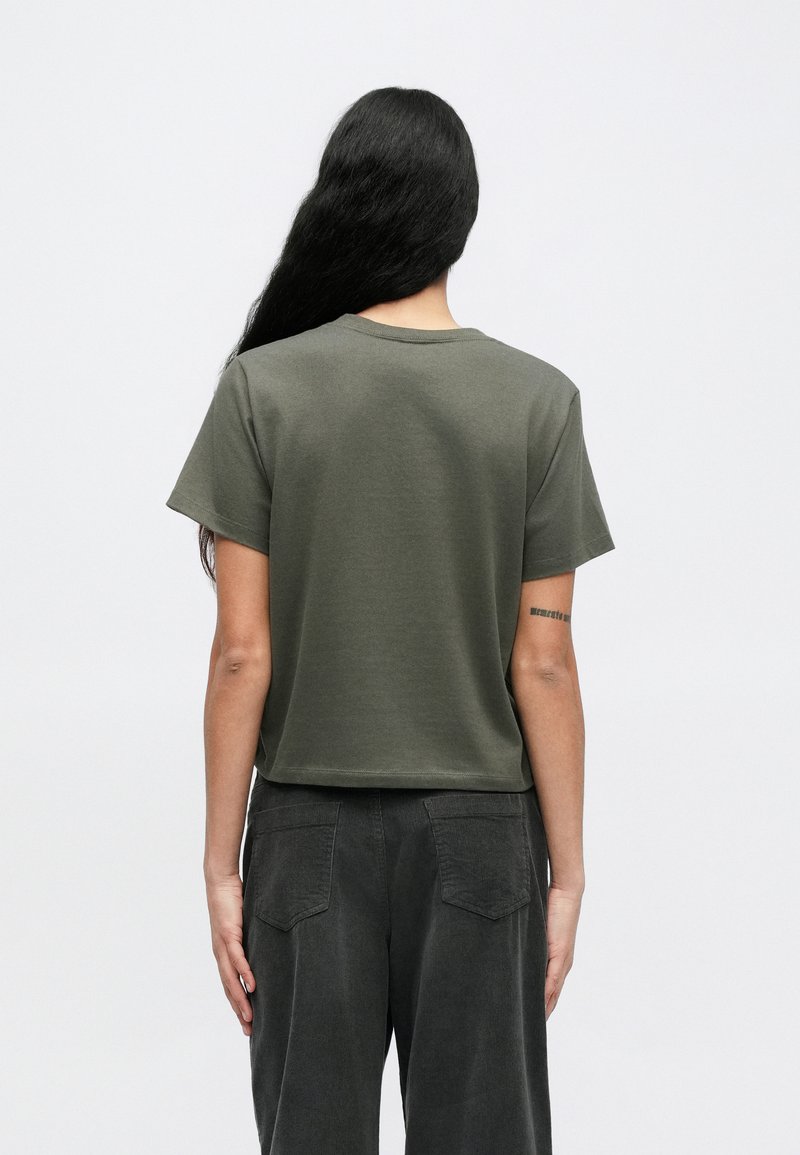 Olive green short-sleeve cotton T-shirt with a relaxed fit and round neckline, paired with dark gray textured corduroy pants.