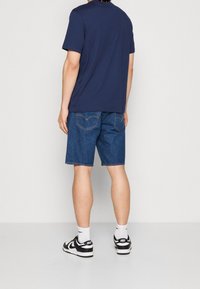 Mörkblå t-shirt med kort ärm, denimshorts, svarta sneakers med vita detaljer. Har en enkel design; shorts har synliga bakfickor.