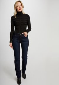 Zwarte geribbelde turtleneck met horizontale strepen, gecombineerd met donkerblauwe slim-fit jeans. Zwarte puntige enkellaarsjes maken de outfit compleet.