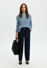 Jasnoniebieski sweter z dzianiny z wysokim kołnierzem, ciemnoniebieskie spodnie o wysokim stanie, czarna torba na ramię i czarne buty wsuwane.