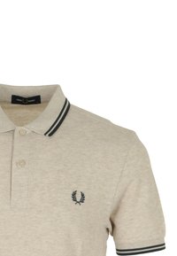 Chemise polo beige en tissu texturé, avec un col à rayures noires et un logo brodé bleu marine sur la poitrine gauche.