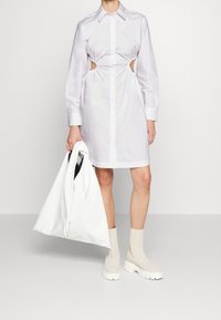 Vit skjortklänning med skärning på sidorna, långa ärmar och draperad tyg. Matchad med en vit väska och beiga ankelstövlar.