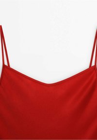 Haut à fines bretelles rouges avec une légère brillance et un décolleté arrondi sur un fond blanc uni.