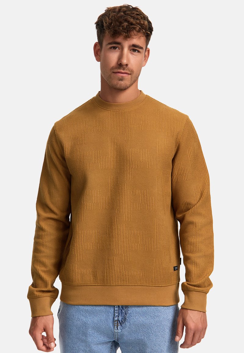 Sudadera de color mostaza con un patrón texturizado, cuello redondo y puños de canalé. Combinada con unos jeans de mezclilla claros, mostrando un aspecto casual.