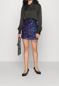 Černá saténová košile s dlouhými rukávy a límečkem, v kombinaci s přiléhavou mini sukní v purpurové a modré barvě posetou flitry a černými vysokými podpatky. Doplňky zahrnují černou tašku.