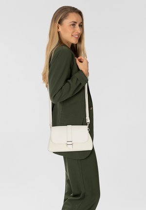 Sac bandoulière en cuir blanc avec une fermeture à rabat, doté d'un accent en métal argenté et d'une sangle réglable. Surface texturée, design compact.