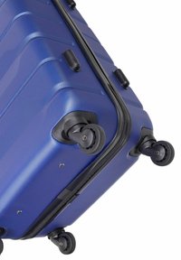 Niebieska walizka twarda z teksturowaną powierzchnią, zaokrąglonymi liniami i czterema czarnymi kółkami. W wyposażeniu zamek i czarne plastikowe akcenty.