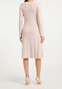 Långärmad, pastellrosa stickad klänning med en figurnära överdel och utsvängd kjol. Har en rund halsringning och en mjuk textur.