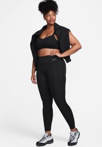 Svart treningsantrekk: sportsbh og høytaljede leggings. Stoffet er glatt med en tettsittende design. Merkelig Nike-logo på leggings.