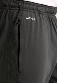Pantalones cortos deportivos Dri-Fit negros con cintura elástica, bolsillo lateral con cremallera y paneles de malla texturizada para transpirabilidad y absorción de humedad.