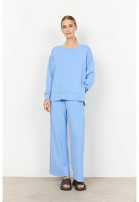 Set di abbigliamento da casa azzurro chiaro realizzato in tessuto morbido; presenta una felpa ampia e pantaloni a gamba larga, abbinati a sandali scivolosi scuri.