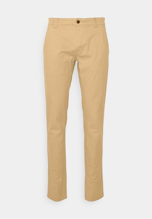 Beige bomuldsbukser med lige ben, der har en frontknap, bæltestropper og en glat tekstur.
