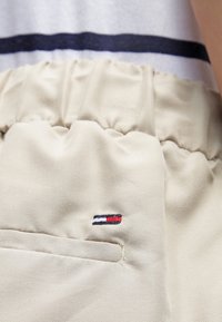 Beige elastic-waist shorts featuring a subtle textured surface and a small, embroidered logo in red, white, and blue on the front pocket.