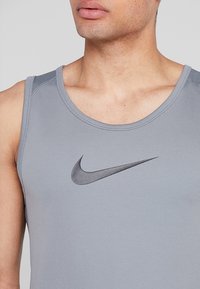 Camiseta deportiva sin mangas de color gris, hecha de un material texturizado, con un logo negro de Nike en el centro y un escote redondo.