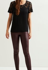 Top nero con maniche corte in pizzo e scollatura rotonda, abbinato a leggings in pelle bordeaux aderenti, creando una silhouette slanciata.