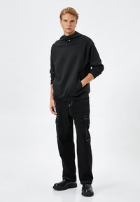 Svart sweatshirt med hög krage och tryckknappar; kombinerat med svarta cargobyxor med kontrasterande vit sömnad och fickor.