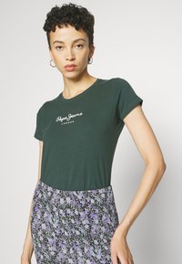 Žalias medvilninis marškinėliai trumpomis rankovėmis, su baltu "Pepe Jeans London" logotipu. Suderinta su gėlių rašto sijonu violetinės ir juodos spalvos.