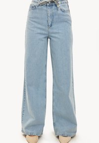 Lichtblauwe, high-waisted, wijd uitlopende jeans gemaakt van denim. Voorzien van een strikdetail aan de voorkant, traditionele zakken en een rafelige zoom.