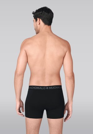 Črne bokser hlačke iz gladkega blaga, z črnim pasom z logotipom »MUCHACHO« v sivi barvi, prikazane od zadaj.