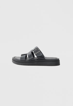 Black slide sandals featuring two crossover straps, a silver buckle accent, and a textured rubber sole for grip.